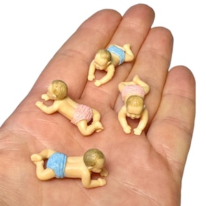 May include: Four miniature plastic baby figurines in a crawling position. Two of the babies wear light blue diapers, and two of the babies wear light pink diapers. Each figurine has molded hair and skin-toned plastic bodies with detailed features.