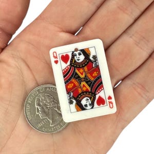 Op de afbeelding: Een miniatuur speelkaart met de Harten Koningin, met rode en zwarte details op een witte achtergrond. De kaart wordt naast een Amerikaanse kwartmunt getoond ter vergelijking. De kaart heeft een klein gaatje aan de bovenkant.