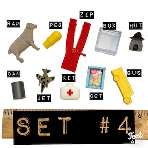 May include: A collection of miniature objects including a beige ram, yellow peg, red zip, clear box, grey hut, grey can, grey jet, white first aid kit with a red cross, blue cot with a figure, and yellow bus, displayed with a 6-inch ruler.
