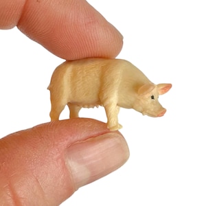 May include: A miniature figurine of a pig in a light beige color. The small animal figure features a textured surface, pointed ears, a snout with pinkish detailing, and a small black eye, captured in a standing position with four legs.