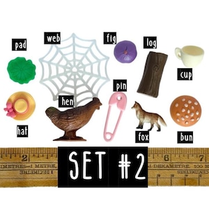May include: A collection of miniature objects labelled set #2, including a green pad, white web, purple fig, brown log, white cup, yellow hat, brown hen, pink pin, brown fox, and a tan bun, positioned above a ruler measuring in centimetres.