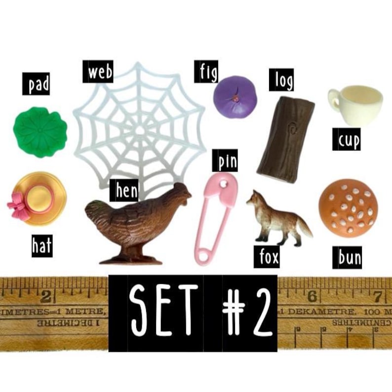 May include: A collection of miniature objects labelled set #2, including a green pad, white web, purple fig, brown log, white cup, yellow hat, brown hen, pink pin, brown fox, and a tan bun, positioned above a ruler measuring in centimetres.