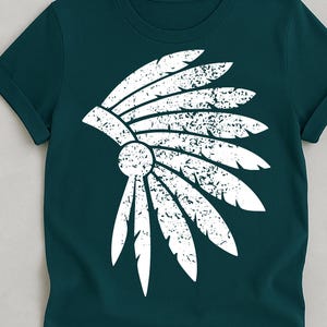 Könnte beinhalten: Dunkelblaues T-Shirt mit einem weißen, abgenutzten Design eines indianischen Kopfschmucks. Die Grafik zeigt stilisierte Federn und ein zentrales kreisförmiges Element. Das T-Shirt hat kurze Ärmel und einen gerollten Saum.