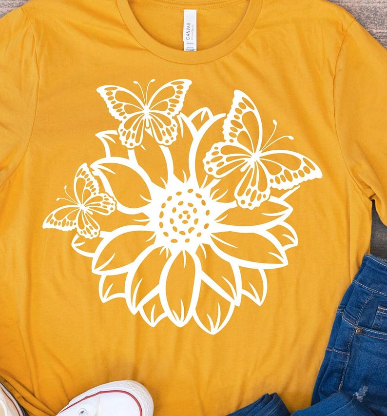 Pode incluir: Uma camiseta amarela mostarda com um gr&aacute;fico branco de um girassol e tr&ecirc;s borboletas.