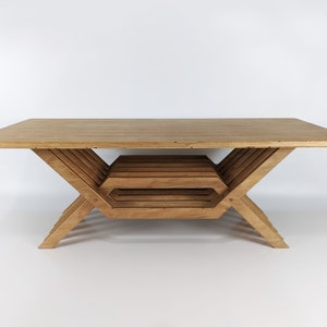 May include: A wooden coffee table with a unique, geometric design. The table has a rectangular top and a base made of multiple intersecting pieces of wood, creating a layered effect.
