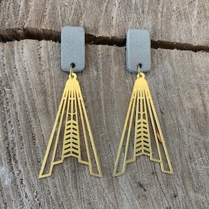 Könnte beinhalten: Ein Paar goldene geometrische Ohrringe mit grauen rechteckigen Oberteilen. Die Ohrringe haben die Form eines Dreiecks mit einem geometrischen Muster.