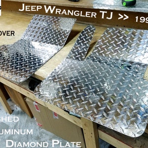 May include: Two silver diamond plate floor mats for a Jeep Wrangler TJ, 1997-2006. The mats are made of highly polished aluminum and are designed to fit the front of the vehicle.  "FRONT FLOOR COVER" and "JEEP WRANGLER TJ >> 1997-2006" are printed on the wooden surface.