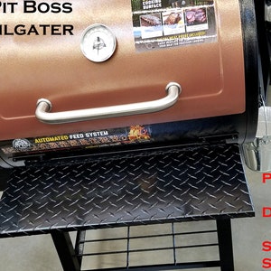 May include: A brown and black Pit Boss Tailgater smoker with a stainless steel handle and a black diamond plate shelf. The smoker has a digital control panel and an automated feed system. The shelf is powder coated aluminium with stainless steel hinges.