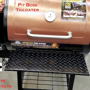 May include: A copper-coloured Pit Boss Tailgater pellet grill with a black base and a folding shelf with stainless steel brackets. The grill has a digital control panel and an automated feed system. The shelf is made of powder-coated aluminium with a diamond plate design.