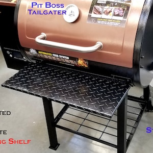 May include: A black and copper Pit Boss Tailgater smoker with a folding shelf. The shelf is made of powder-coated aluminium with a diamond plate design. The smoker has a stainless steel hinge and a small metal bucket.