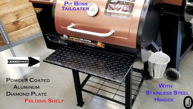 May include: A black and copper Pit Boss Tailgater smoker with a folding shelf. The shelf is made of powder-coated aluminium with a diamond plate design. The smoker has a stainless steel hinge and a small metal bucket.