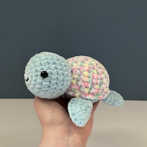 May include: A crocheted blue turtle toy with a colourful shell. The shell is made of a variety of pastel colours, including pink, yellow, and green.