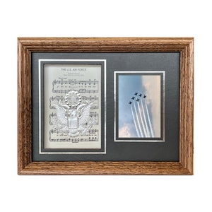 May include: A framed print of the U.S. Air Force seal with sheet music and a photo of the Thunderbirds air show team flying in formation.