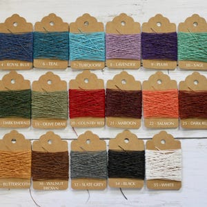 May include: A selection of twine spools in various colours, each with a label indicating the shade. Colours include Royal Blue, Teal, Turquoise, Lavender, Plum, Sage, Dark Emerald, Olive Drab, Country Red, Maroon, Salmon, Dark Rust, Butterscotch, Walnut Brown, Slate Grey, Black, and White.