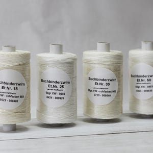 Puede incluir: Cuatro carretes de hilo de encuadernación blanquecino, cada uno con una etiqueta blanca que muestra texto. Los carretes están etiquetados Et.Nr. 18, 25, 30 y 50. El hilo está enrollado alrededor de un núcleo cilíndrico. El fondo es gris claro.