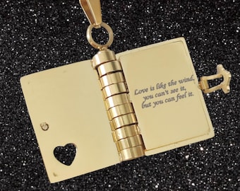 May include: Gold-toned necklace with a book-shaped pendant that opens to reveal an engraved message: "Love is like the wind, you can't see it, but you can feel it."