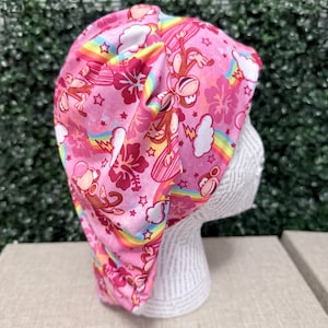 Peut inclure: Une charlotte de bloc rose avec un motif répétitif de singes bruns, d'arcs-en-ciel vibrants, de nuages blancs et de fleurs d'hibiscus rose foncé. Le tissu présente un design froncé avec une texture douce et un imprimé coloré sur fond rose.