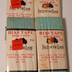 May include: Several packages of vintage bias tape from Fruit of the Loom. The packaging is cream-colored with red text and a fruit illustration. The tape itself is a light teal color. The packaging includes the text "BIAS TAPE DOUBLE FOLD".