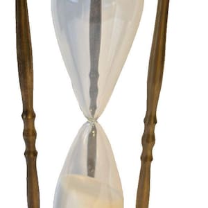 May include: An hourglass featuring a brass frame with three vertical supports and spherical finials. The clear glass bulbs are connected by black collars and contain white sand, which is currently flowing from the top bulb to the bottom bulb.
