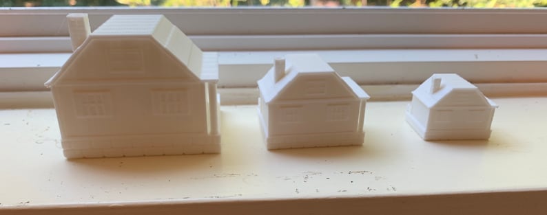 May include: Three white 3D printed model houses of different sizes. The houses are all simple in design with a pitched roof and a single window on each side.