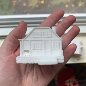 May include: A white 3D printed model of a small house with a porch and windows.