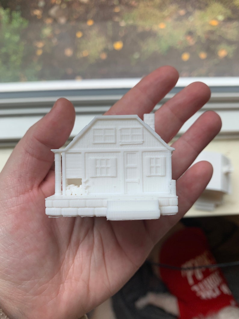 May include: A white 3D printed model of a small house with a porch and windows.