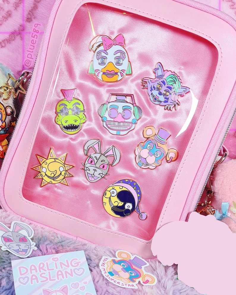 May include: A pink zippered pouch with a clear plastic window displaying a collection of colorful enamel pins featuring cartoon characters. The pins are themed around a popular video game. The pouch is sitting on a fluffy pink and purple surface.