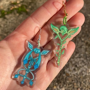 May include: A pair of clear acrylic earrings with colourful designs. One earring features a blue and white design with a heart and a bow. The other earring features a green and yellow design with a heart and leaves.