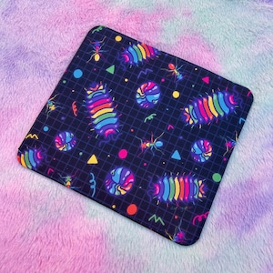 May include: A black mouse mat with a retro 80s design featuring colourful rainbow-coloured worms, ants, and geometric shapes on a black grid background.