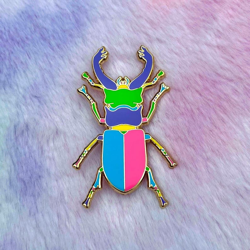 Peut inclure: Une &eacute;pingle en forme de scarab&eacute;e dor&eacute;e avec un motif bleu, rose et vert. Le scarab&eacute;e a de grandes mandibules pointues et un corps segment&eacute;.