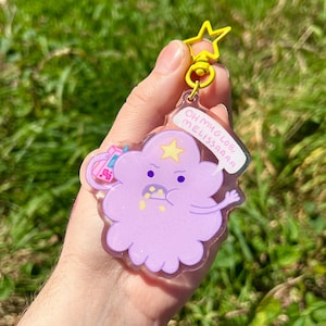May include: A purple and pink glitter keychain featuring a cartoon character with a star on its head. The character is saying "Oh my glob, Melissa!"