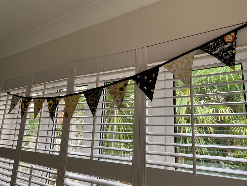 Bee Lovers Honey Hive Inspirational Quote Bee Kind Sunflower Black and Yellow Cotton Fabric Bunting by Bluebell Bunting. Small bunting in a window display, draped from the lintel, against white shutters.