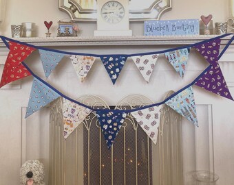 May include: A double-layered fabric bunting banner featuring triangular flags with various British-themed patterns, including Union Jacks, crowns, teapots, and London landmarks, all connected by a solid dark blue fabric trim and hanging in two rows.