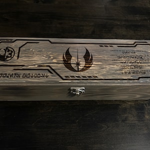 May include: A wooden box with a latch, featuring a laser-engraved Star Wars Jedi Order symbol and text in Aurebesh, the fictional language of Star Wars.