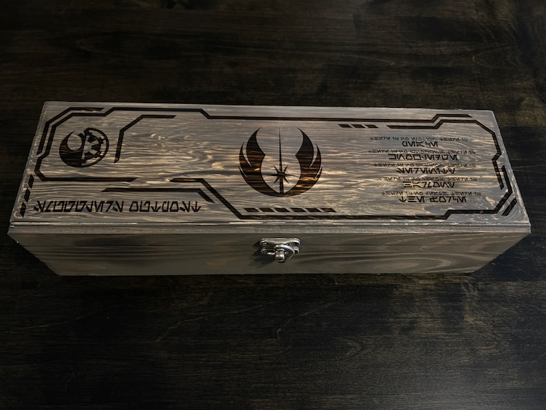 May include: A wooden box with a latch, featuring a laser-engraved Star Wars Jedi Order symbol and text in Aurebesh, the fictional language of Star Wars.