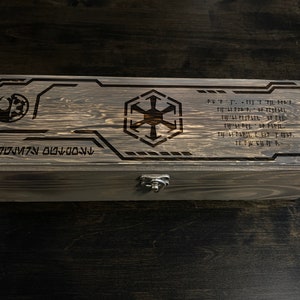 May include: A wooden box with a dark brown stain. The top of the box has a laser-engraved design featuring the Star Wars Rebel Alliance symbol and the Imperial symbol. The box also has a metal latch.