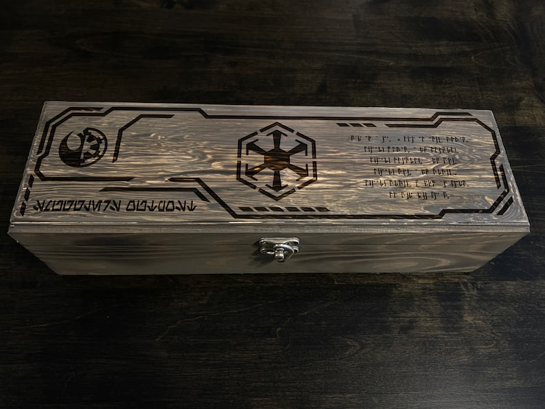 May include: A wooden box with a dark brown stain. The top of the box has a laser-engraved design featuring the Star Wars Rebel Alliance symbol and the Imperial symbol. The box also has a metal latch.