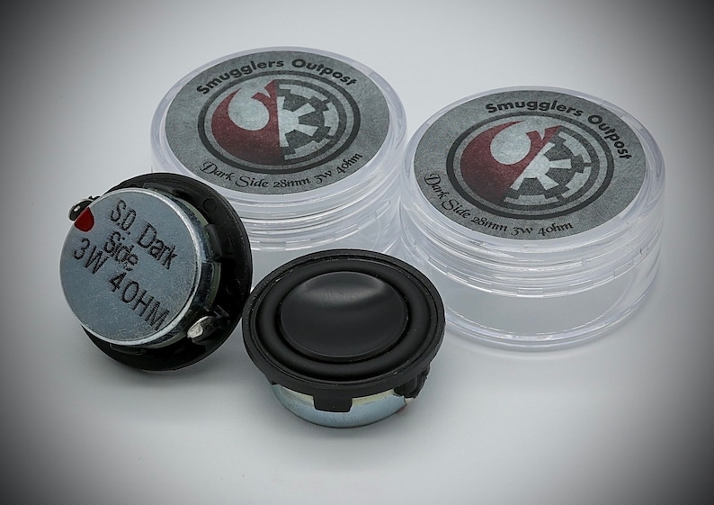 May include: Two small, black, round speakers with a silver label that reads "S.O. Dark Side 3W 40HM". The speakers are in front of two clear plastic containers with labels that read "Smugglers Outpost Dark Side 28mm 3W 4ohm".