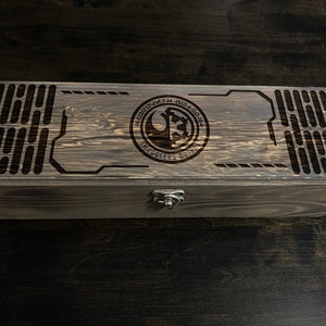 May include: A wooden box with a dark brown finish. The top of the box has a laser-engraved design featuring a Rebel Alliance symbol and the text "Smugglers Run".