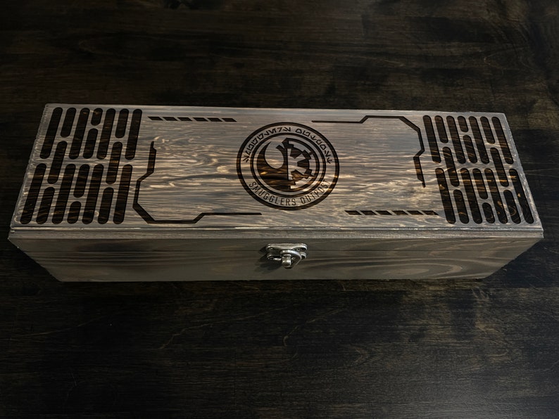 May include: A wooden box with a dark brown finish. The top of the box has a laser-engraved design featuring a Rebel Alliance symbol and the text "Smugglers Run".