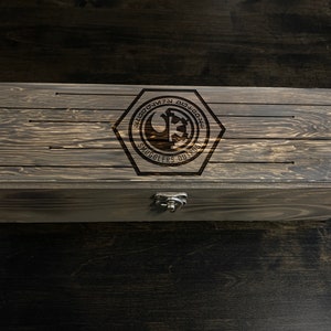 May include: A wooden box with a dark brown stain. The lid has a hexagonal emblem with the text "Smugglers Outpost" and a Rebel Alliance symbol.