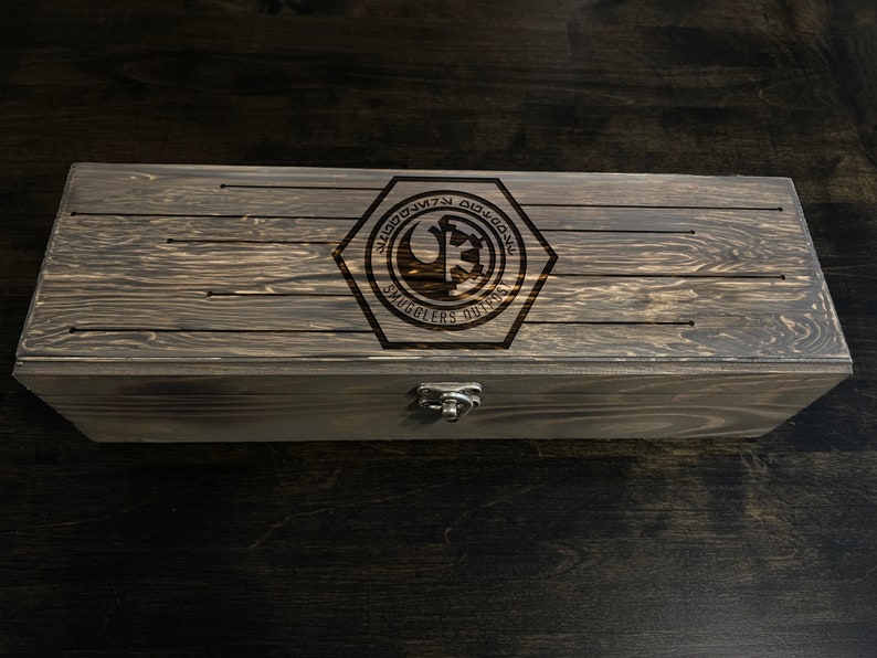 May include: A wooden box with a dark brown stain. The lid has a hexagonal emblem with the text "Smugglers Outpost" and a Rebel Alliance symbol.