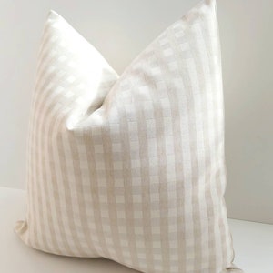 May include: A beige and white gingham pillow cover. The pillow cover is made of a soft, woven fabric with a subtle sheen.