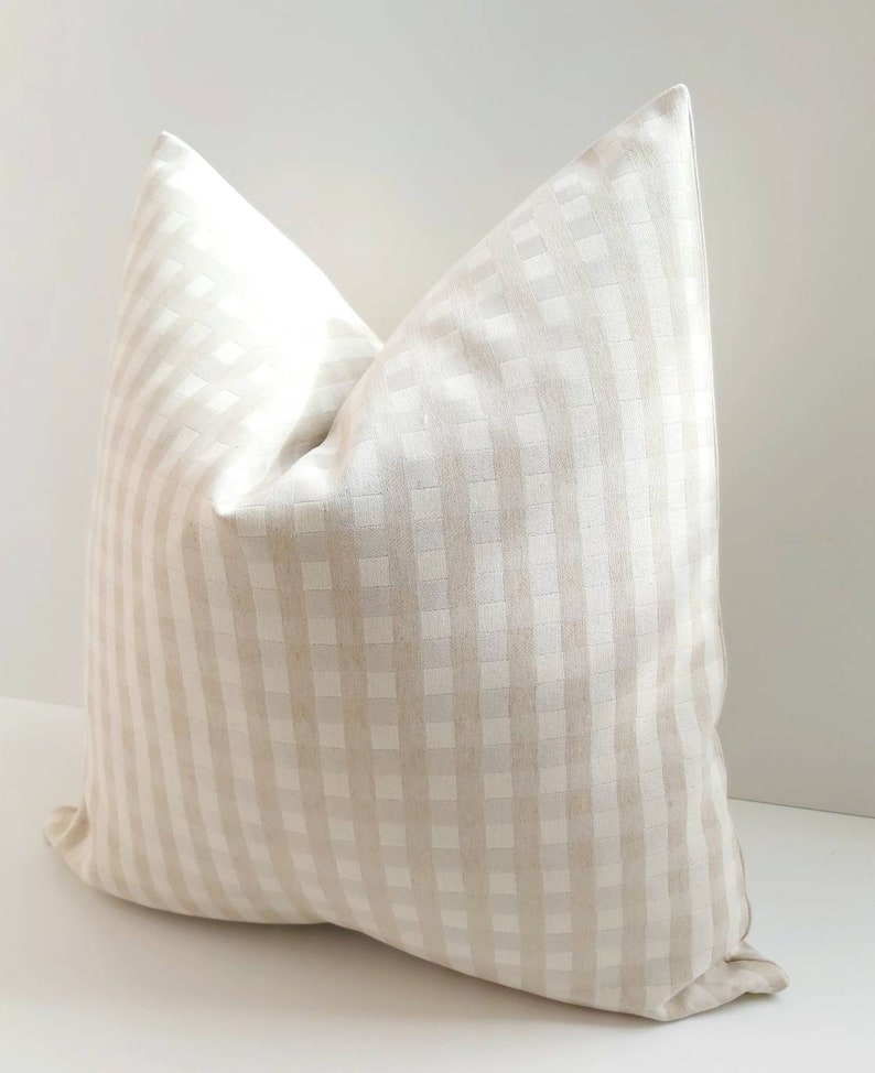 May include: A beige and white gingham pillow cover. The pillow cover is made of a soft, woven fabric with a subtle sheen.