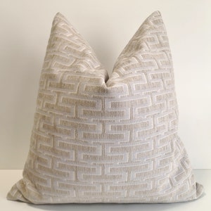 May include: A beige throw pillow with a white geometric pattern. The pillow is made of a soft, textured fabric.