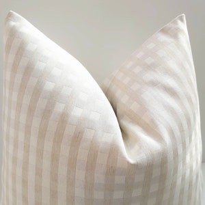 May include: A white and beige checkered pillow cover with a subtle woven texture. The pillow cover is made of a soft, natural fabric and has a simple, elegant design.