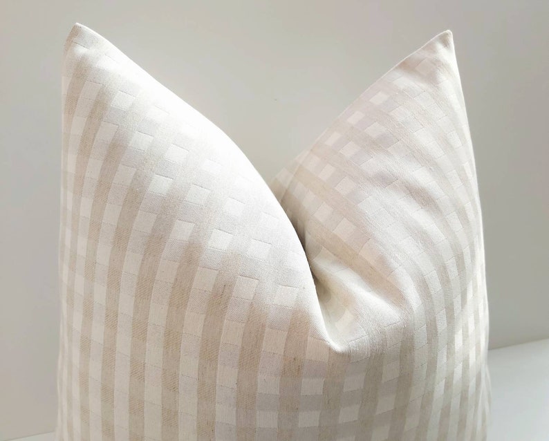 May include: A white and beige checkered pillow cover with a subtle woven texture. The pillow cover is made of a soft, natural fabric and has a simple, elegant design.