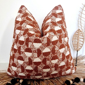 Op de afbeelding: Een bruin en wit gepatroneerd kussen met een geometrisch ontwerp. Het kussen is gemaakt van een textuurstof en heeft een vierkante vorm.