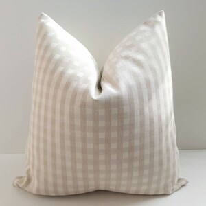 May include: A beige and white gingham pillow cover. The pillow cover is made of a soft, textured fabric and has a subtle sheen.