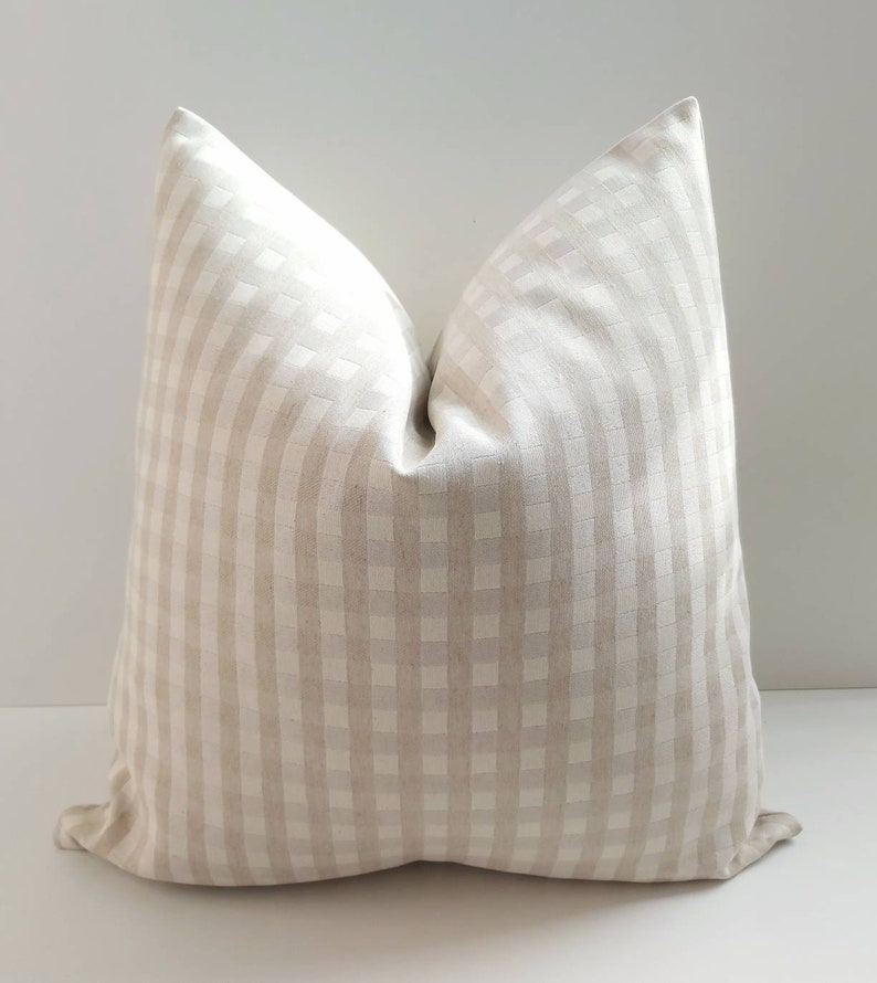 May include: A beige and white gingham pillow cover. The pillow cover is made of a soft, textured fabric and has a subtle sheen.